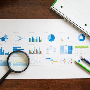 Overhead view of charts and graphs with magnifying glass and stationery on wooden table.